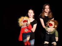Dwie dziewczynki na scenie prezentują  lalki teatralne
