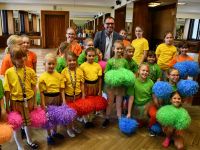 grupa dziewczynek z  kolorowymi pomponami do tańca pozuje do zdjęcia z Dyrektorem Pałacu Młodzieży panem Bartłomiejem Krynickim