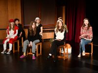 grupa aktorów siedząca na krzesłach na proscenium